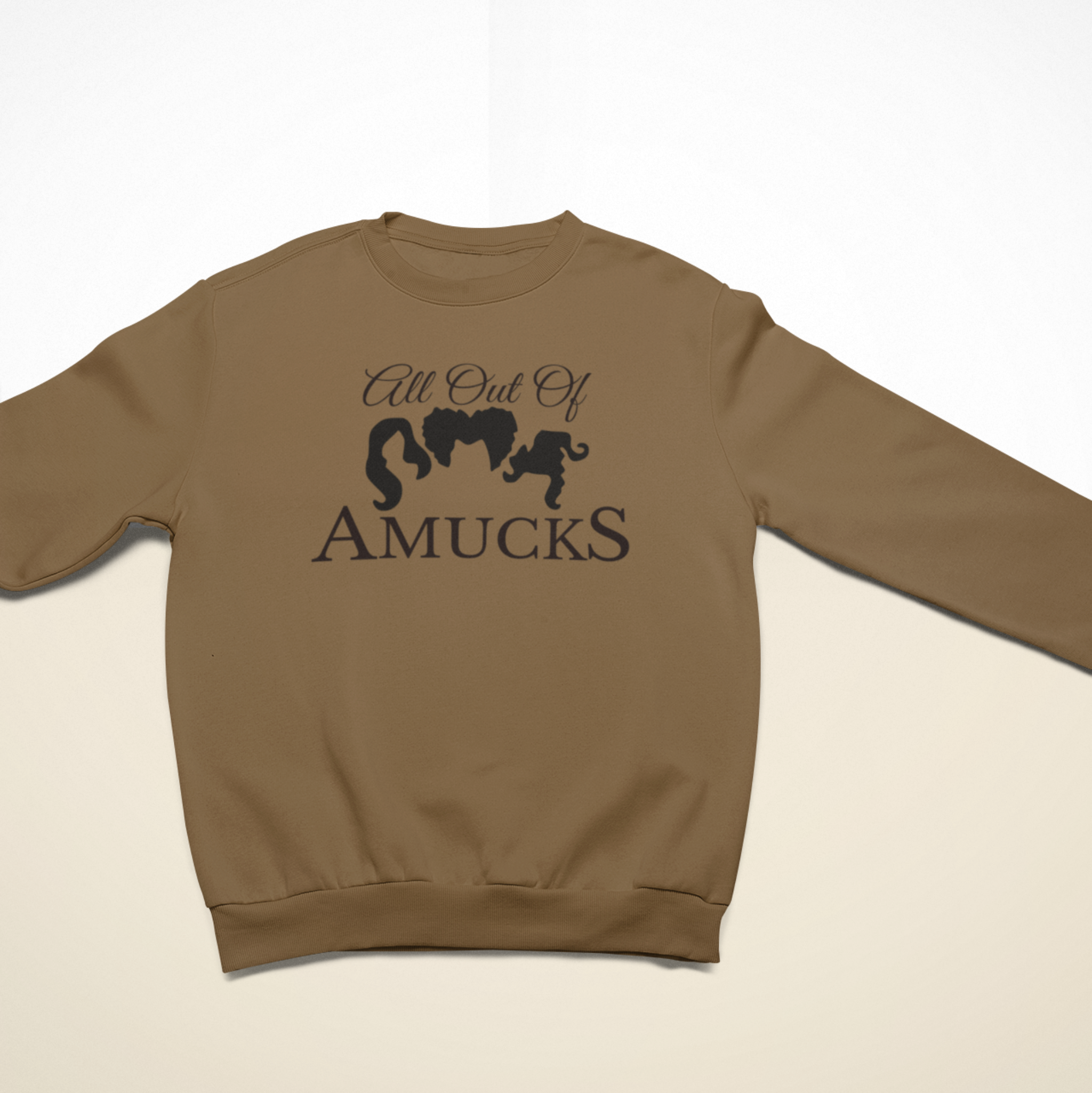 Brown cozy sweatshirt with the phrase "All Out of Amucks" featuring silhouettes of three witches' hairstyles, ideal for Halloween or witch-themed apparel.