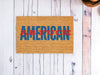 A rectangular doormat with a textured, brown surface bears the phrase "AMERICAN AS F*CK" in bold blue and red letters. Perfect as Memorial Day decor, these 'American As F*ck' Funny Doormats are placed on a white, wooden floor with visible grains and knots. The letters "AS F*CK" are overlaid in red on the word "AMERICAN.