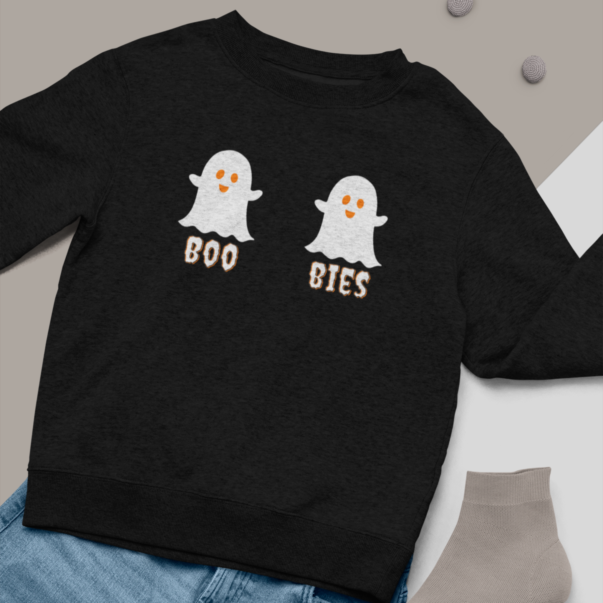 Black cozy Halloween sweatshirt featuring two cute ghost illustrations with the playful text "BOO BIES," styled with blue jeans and gray socks, perfect for casual festive wear.