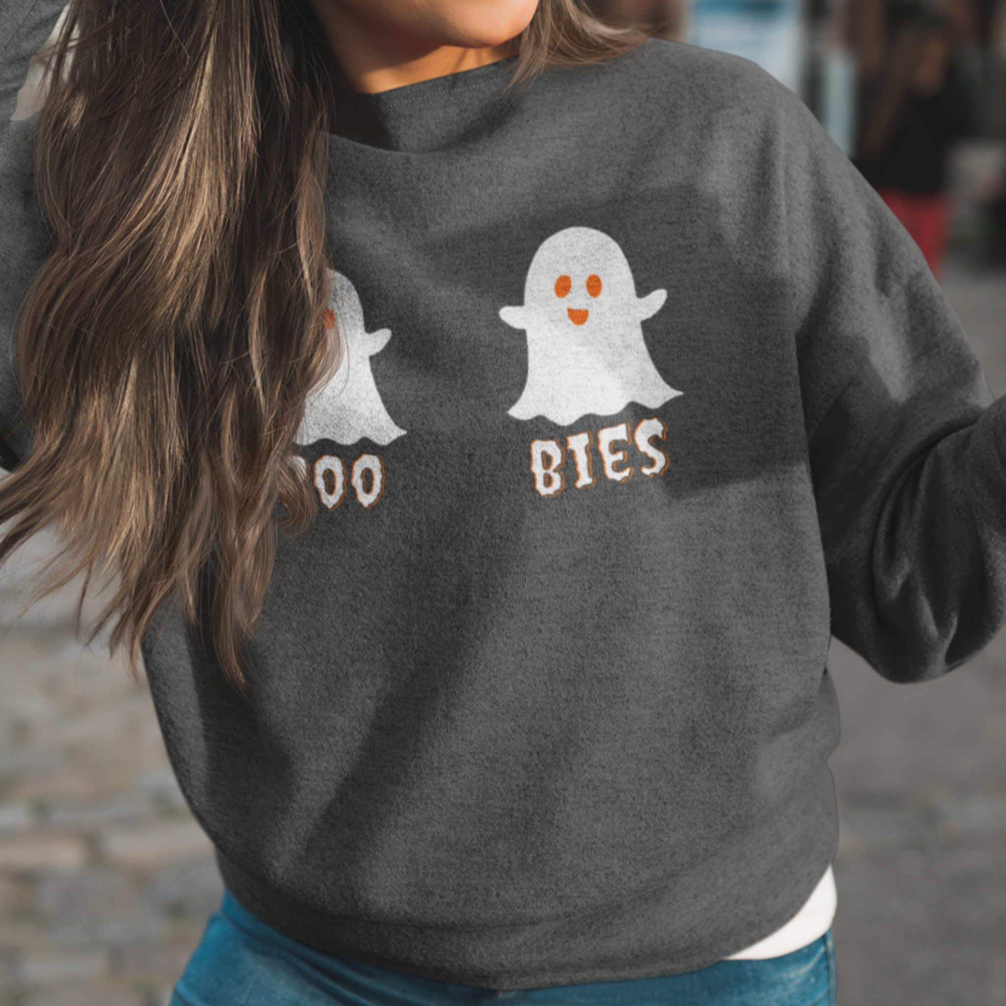 Woman wearing a dark gray cozy Halloween sweatshirt with two cute ghost illustrations and the playful text "BOO BIES," holding a coffee cup outdoors, perfect for casual festive outings.