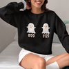 Person wearing a black cozy Halloween sweatshirt featuring two cute ghost illustrations with the playful text "BOO BIES," paired with white shorts and socks, perfect for casual festive lounging.