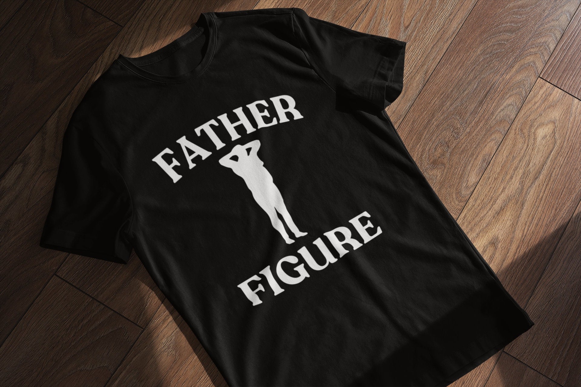 A black shirt laying flat with the phrase 'Father Figure,' making it a funny and custom Father's Day gift for dads. Perfect for those looking for unique and humorous dad shirts.