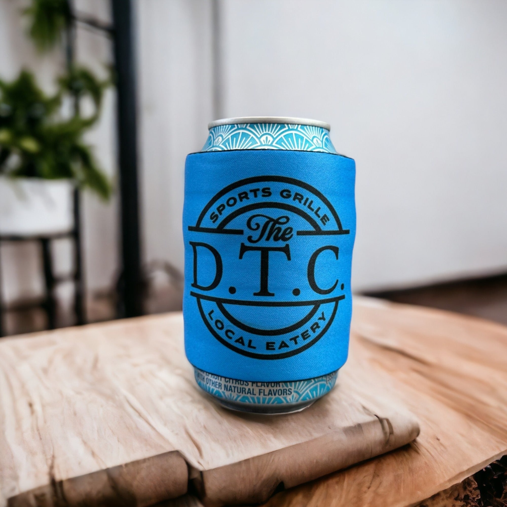 Blue slap wrap drink sleeve with "The D.T.C. Sports Grille Local Eatery" logo, wrapped around a canned beverage, displayed on a wooden table, ideal for custom beverage holders and promotional items.