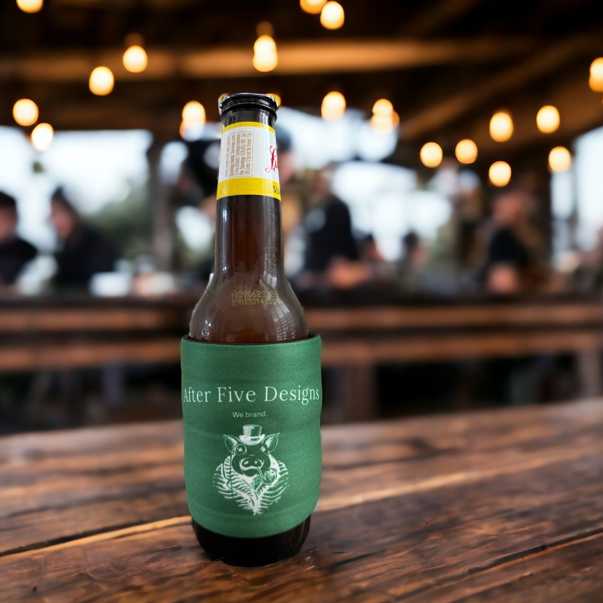 Beer bottle wrapped in a green slap wrap drink sleeve featuring the "After Five Designs" logo, placed on a rustic wooden table with blurred string lights and people in the background, perfect for promotional drink sleeves and branded merchandise.